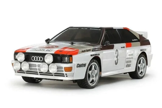 A Tamiya 1/10 scale Audi Quattro Rallye A2 4WD model kit, predominantly white with orange and black detailing, displayed on a plain background.