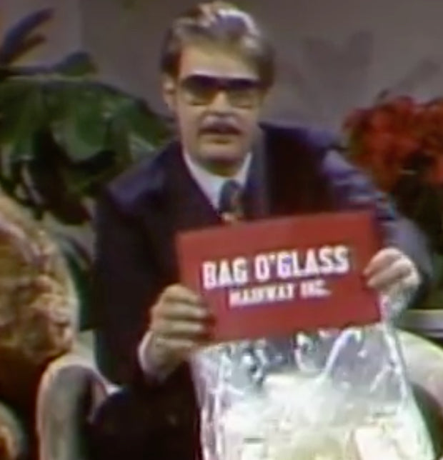 Man holding a 'Bag O'Glass' sign with plants in the background
