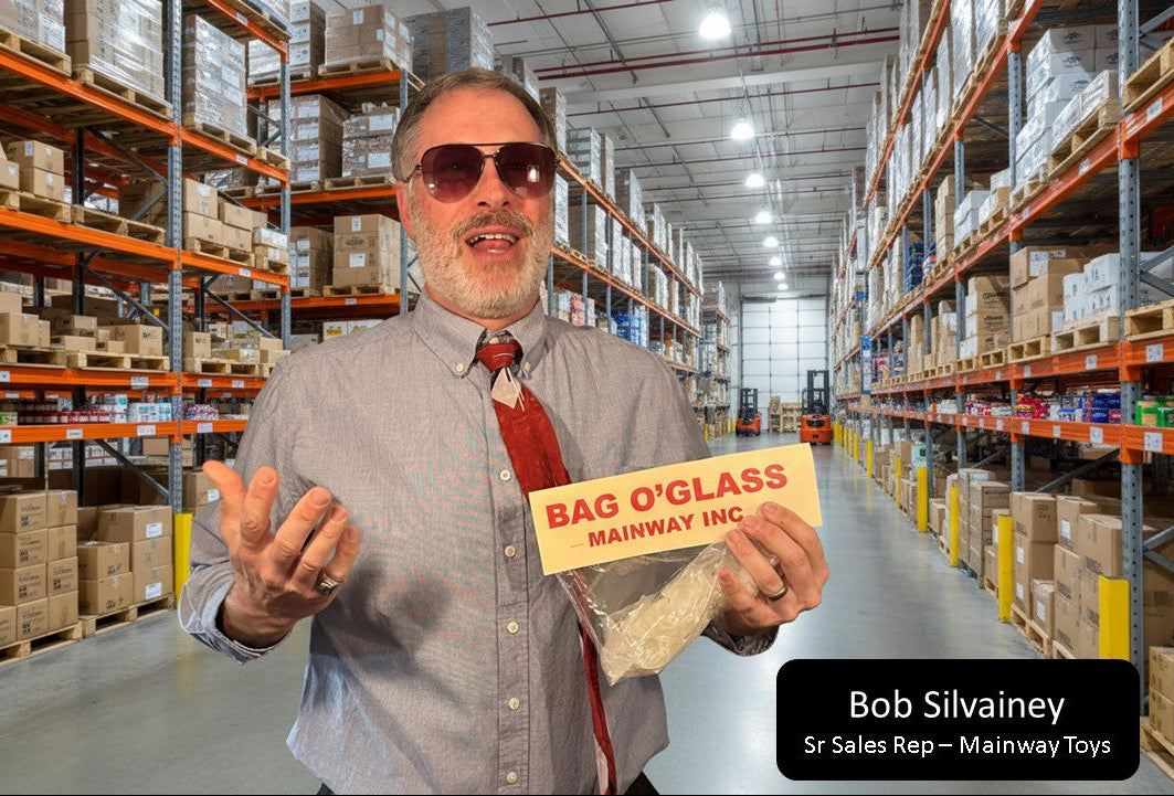 Man in a warehouse holding a sign with 'Bag O'Glass' and 'Mainway Inc.'